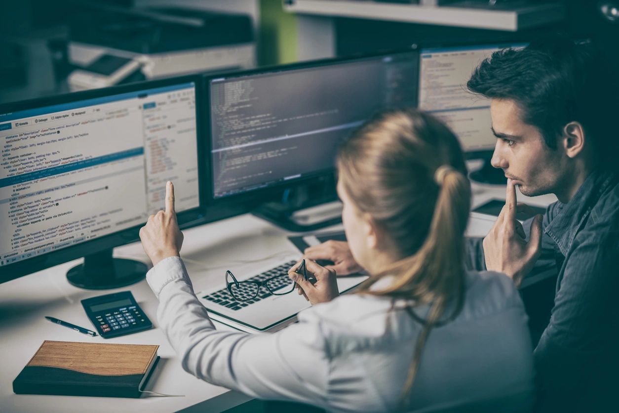 Two people using a computer with three monitors